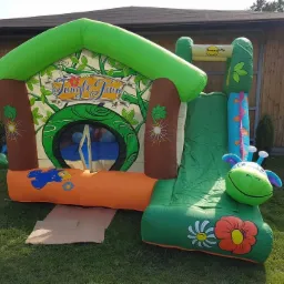 Kolorowy, dmuchany zamek ze zjeżdżalnią w motywie dżungli, z napisem 'Jungle Fun', ustawiony na trawie, z balonami w tle.