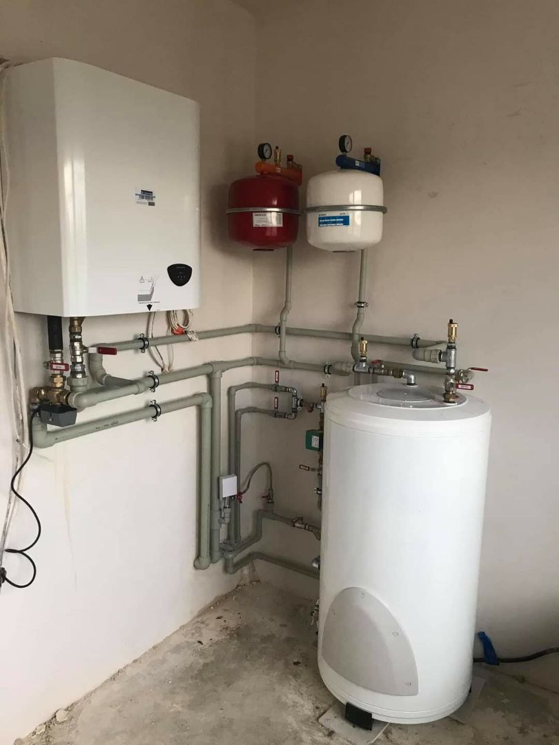 Nowoczesny, biały piec gazowy kondensacyjny z podłączonym zasobnikiem ciepłej wody i dwoma naczyniami przeponowymi w kotłowni o surowym wykończeniu.