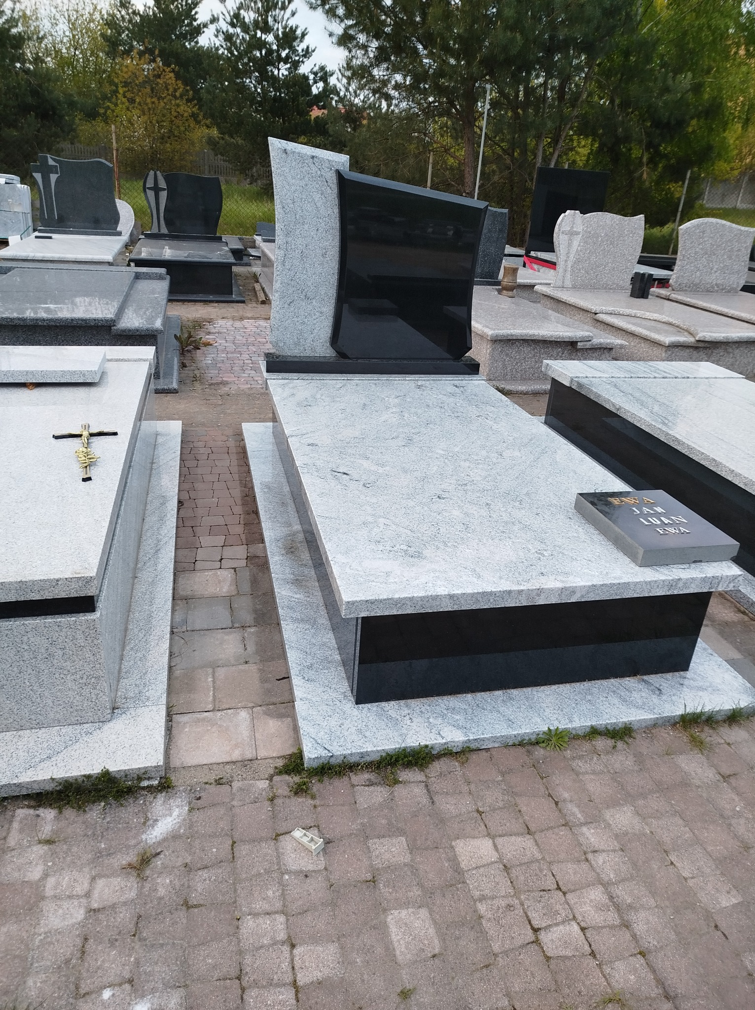 Ekspozycja nagrobków z granitu i czarnego kamienia, z widocznym napisem na jednym z nich, ustawionych na brukowanym placu.