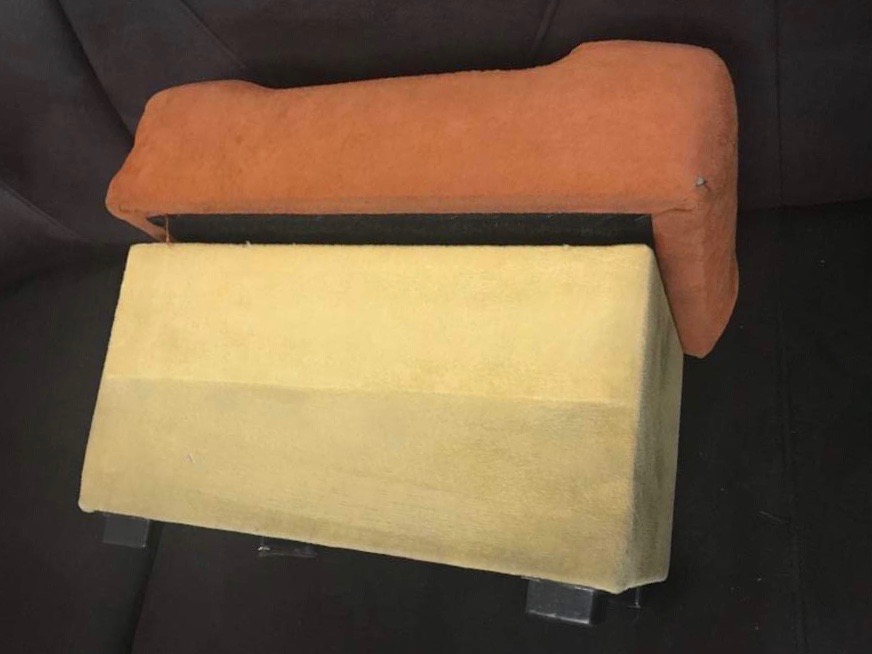 Pomarańczowy podłokietnik kanapy leżący na żółtym siedzisku kanapy z widocznymi nóżkami na ciemnym tle.