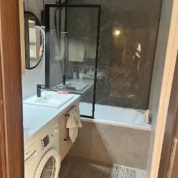 Nowoczesna łazienka w szarościach z kabiną prysznicową typu walk-in, umywalką nablatową, okrągłym lustrem i pralką Bosch Maxx 5.