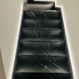 Schody wyłożone czarnym marmurem z białymi żyłami, podświetlone ledowym oświetleniem wzdłuż ściany.