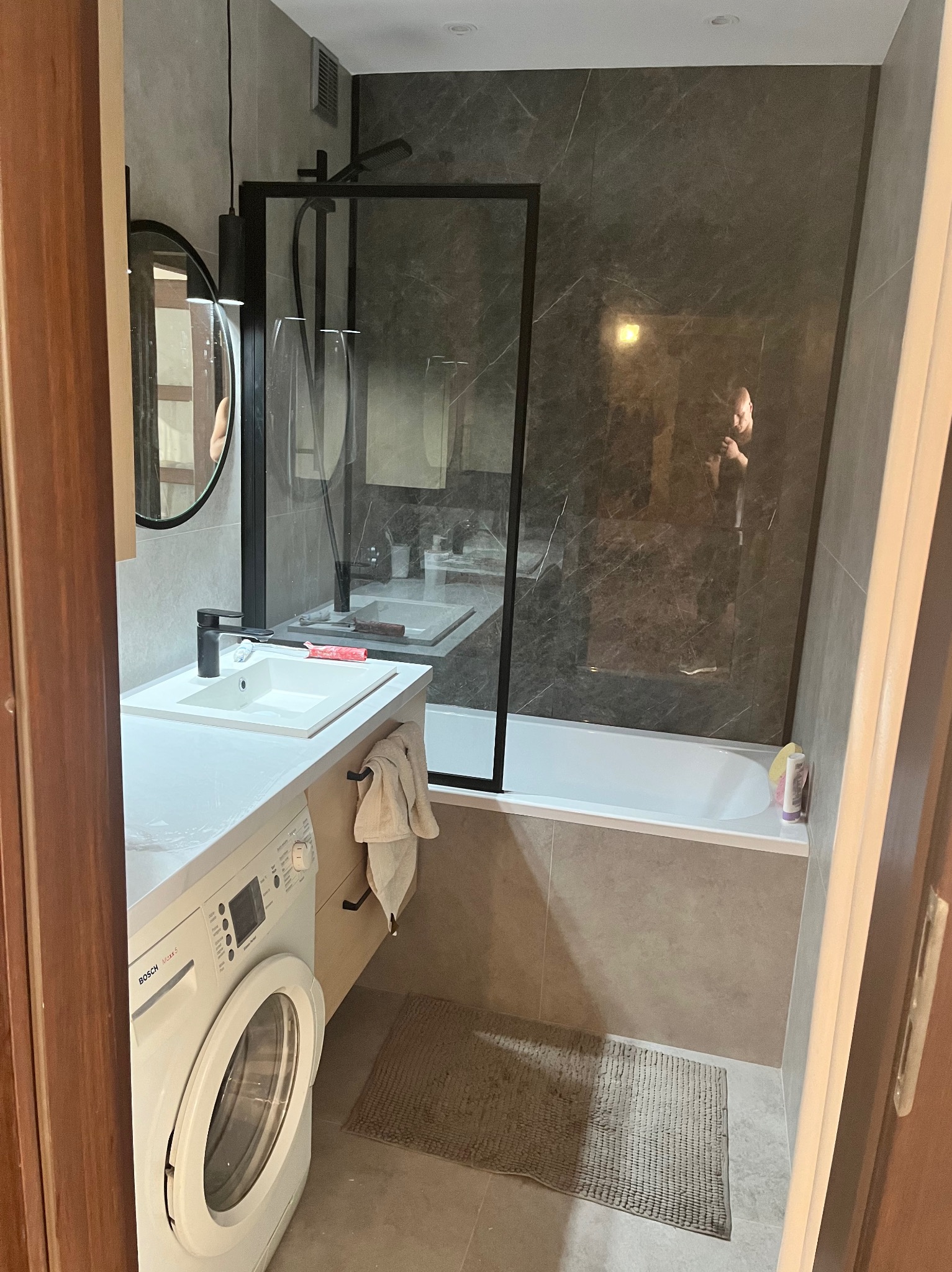 Nowoczesna łazienka w szarościach z kabiną prysznicową typu walk-in, umywalką nablatową, okrągłym lustrem i pralką Bosch Maxx 5.