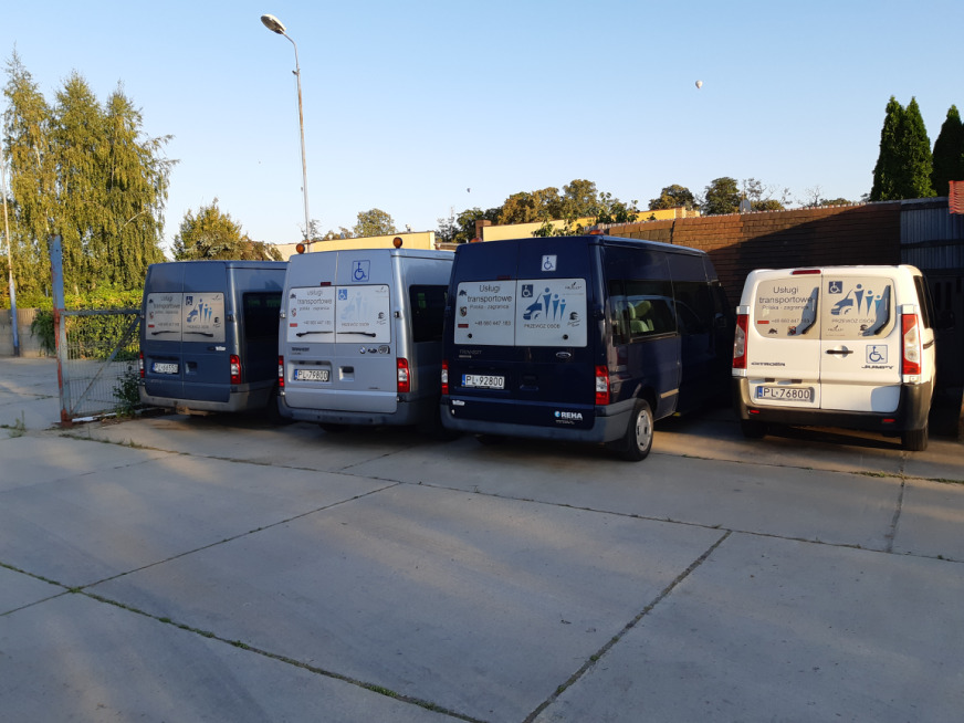 Cztery busy różnych marek i kolorów zaparkowane obok siebie, z widocznymi oznaczeniami o przystosowaniu do przewozu osób niepełnosprawnych, w tym osób na wózkach inwalidzkich. Na każdym busie...