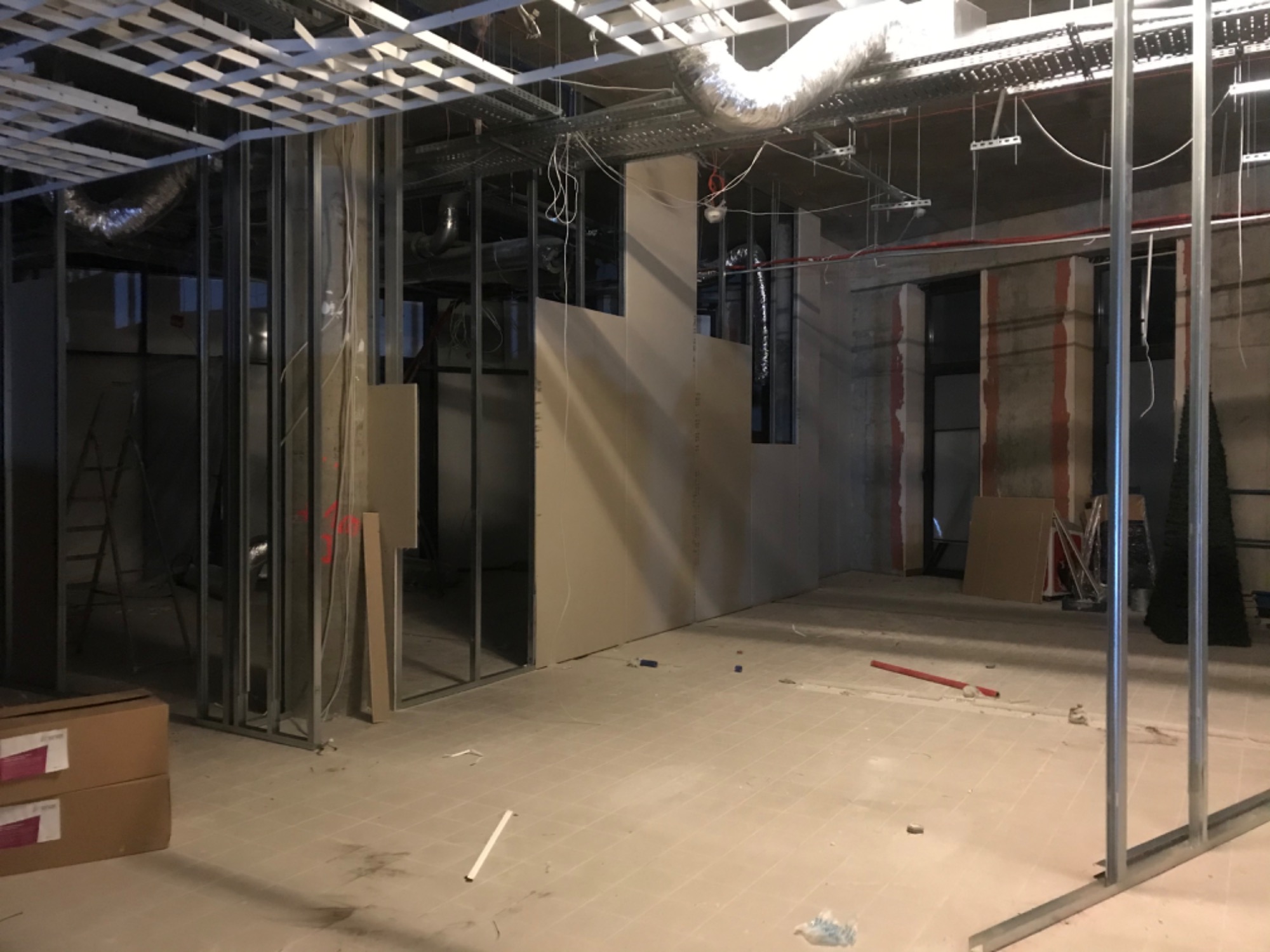 Wnętrze w trakcie montażu ścian działowych z płyt karton-gips, widoczne metalowe profile, częściowo zamontowane płyty, instalacje pod sufitem oraz kartony na podłodze.