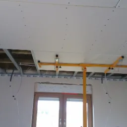 Montaż sufitu podwieszanego z płyty gipsowo-kartonowej, widoczne profile, konstrukcja nośna i podnośnik do płyt.