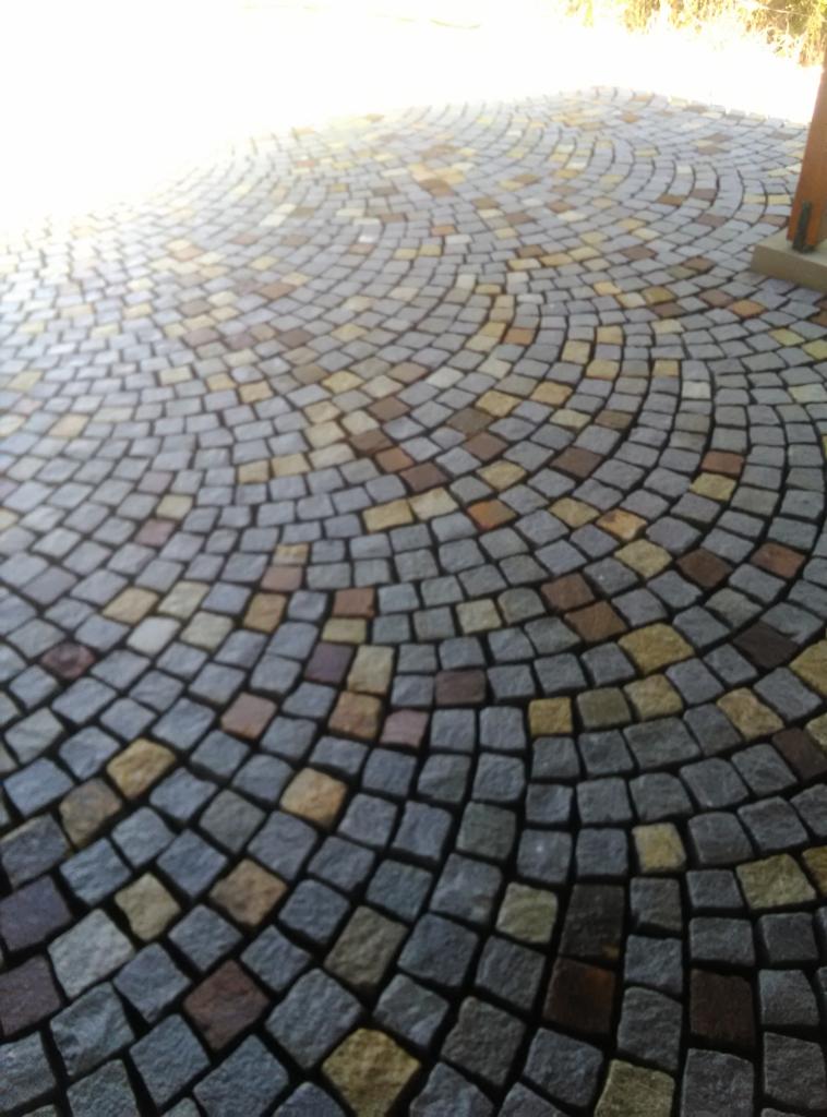 Ułożona okręgami kostka granitowa w odcieniach szarości, brązu i żółci, tworząca wzór wachlarza.