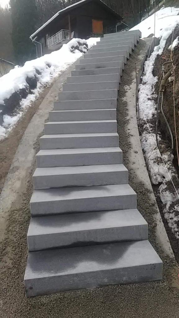 Zewnętrzne schody z szarego kamienia prowadzące pod górę w kierunku domu, częściowo pokryte śniegiem.
