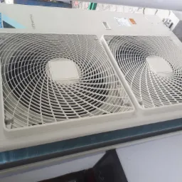 Biała zewnętrzna jednostka pompy ciepła Daikin Altherma z dwoma wentylatorami, zamontowana na zewnątrz budynku, widoczna z góry pod kątem.