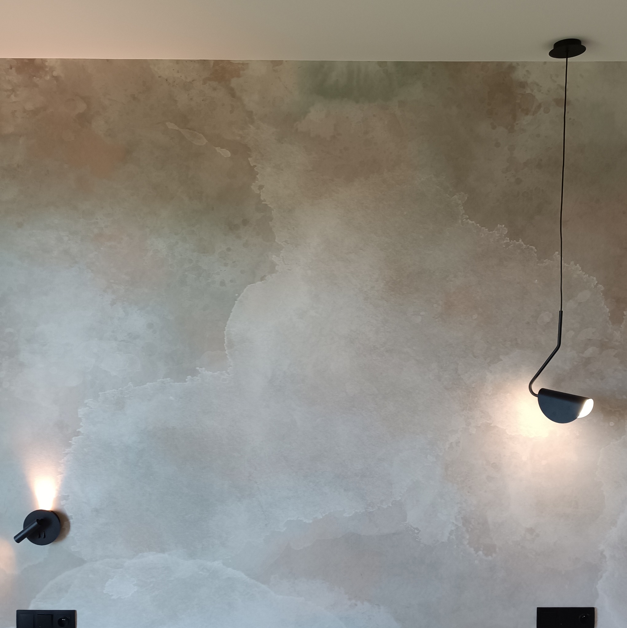 Ściana z efektem dekoracyjnym imitującym chmurę, oświetlona dwoma czarnymi lampami: ścienną i wiszącą.