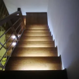 Schody drewniane z podświetleniem LED pod stopniami, widok od dołu, balustrada metalowa.
