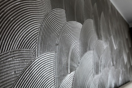 Dekoracyjna ściana z szarego tynku strukturalnego, wzór półokręgów z wyraźnymi żłobieniami, widok z boku.