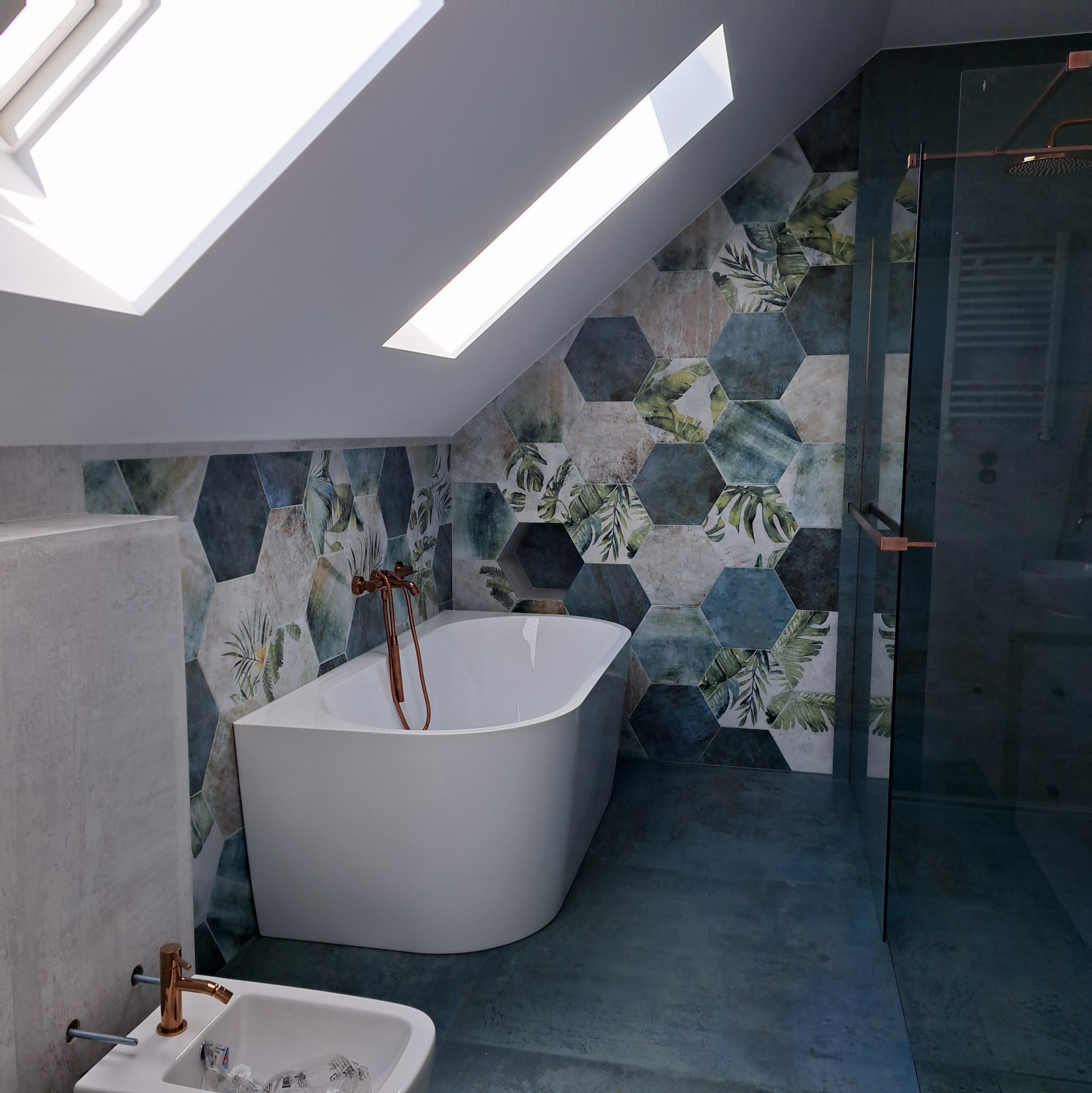 Nowoczesna łazienka na poddaszu z heksagonalnymi płytkami w odcieniach zieleni i błękitu, wolnostojąca wanna i kabina prysznicowa z miedzianymi akcentami.
