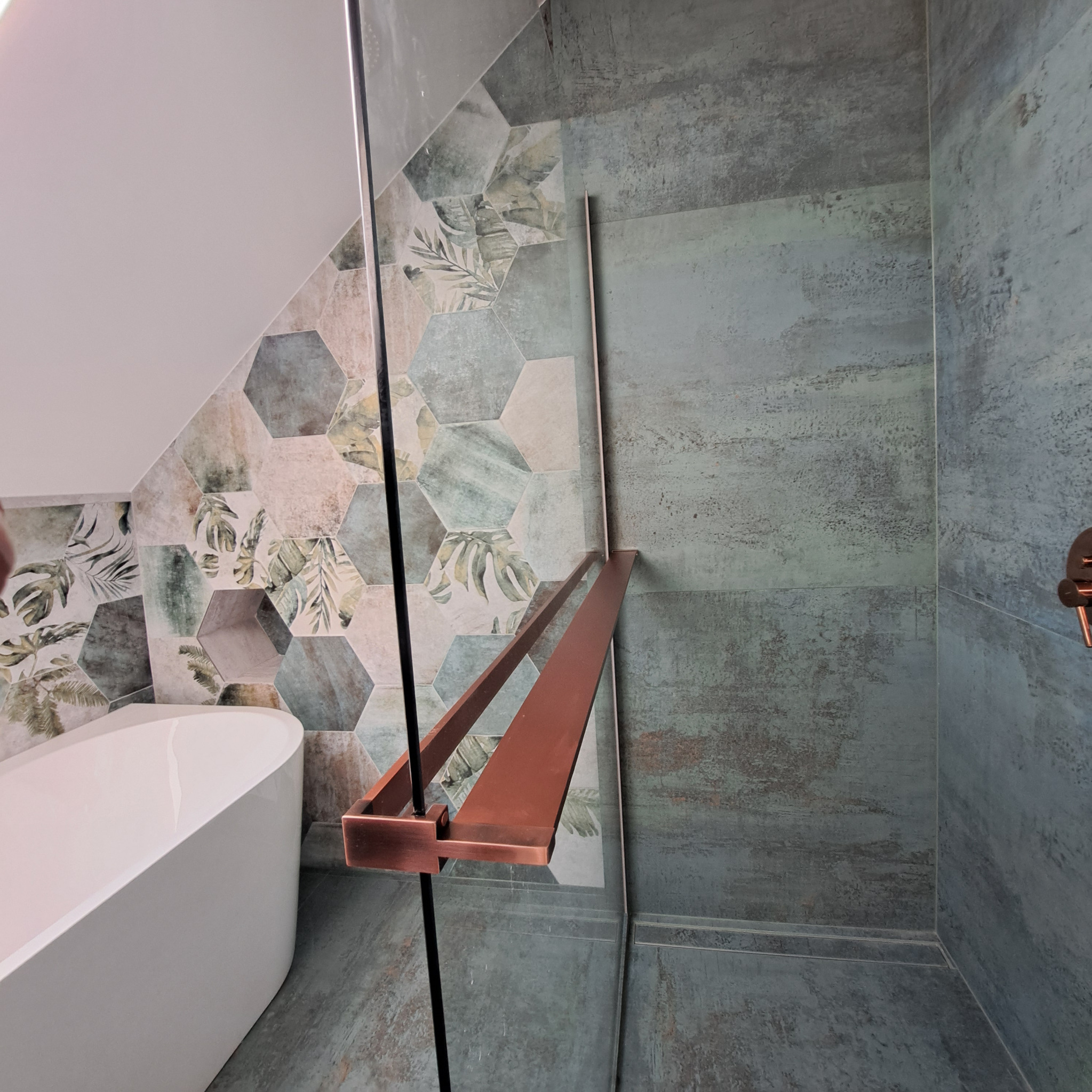 Nowoczesna łazienka z wanną i kabiną prysznicową. Ściany wyłożone heksagonalnymi płytkami z motywem roślinnym i szarymi płytami imitującymi beton.