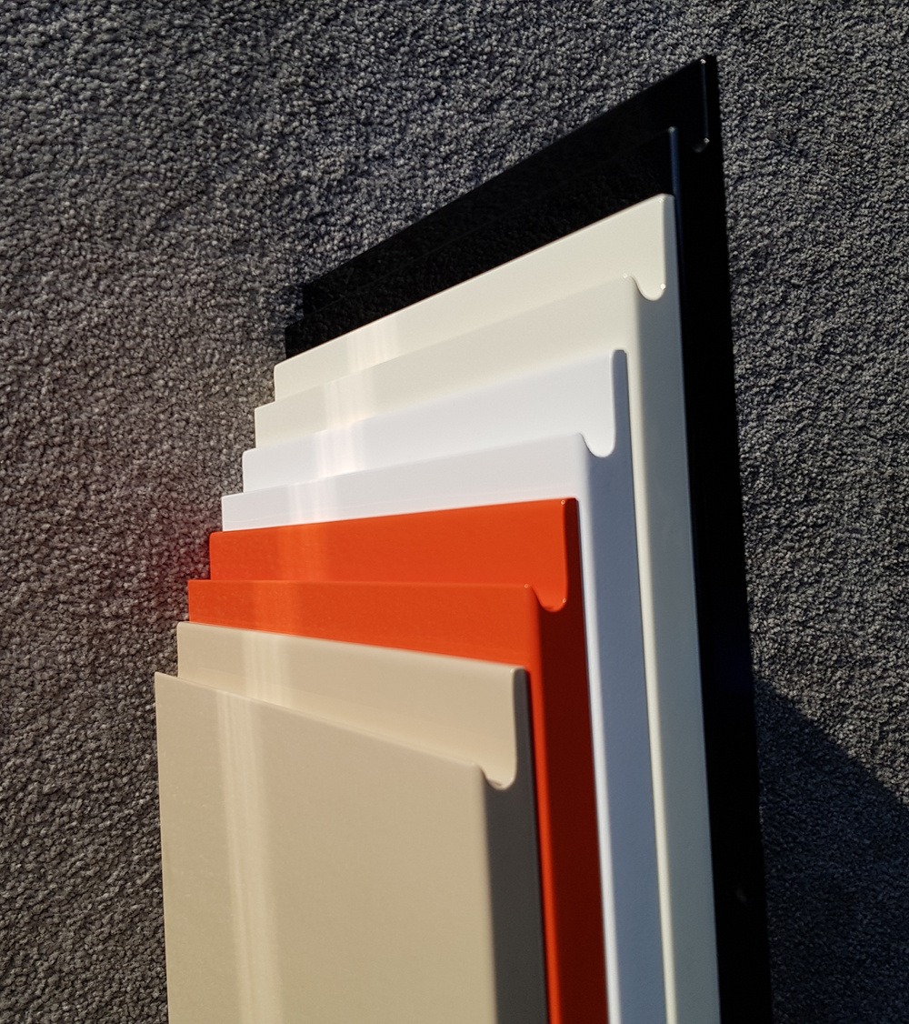 Przekrój profili meblowych w odcieniach beżu, pomarańczy, bieli i czerni, ukazujący różnorodność kolorów i wykończeń na tle szarej, chropowatej ściany.