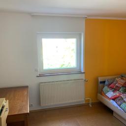 Pobrzut - Jasny pokój z pomarańczową ścianą, białym grzejnikiem pod oknem i patchworkową narzutą na łóżku