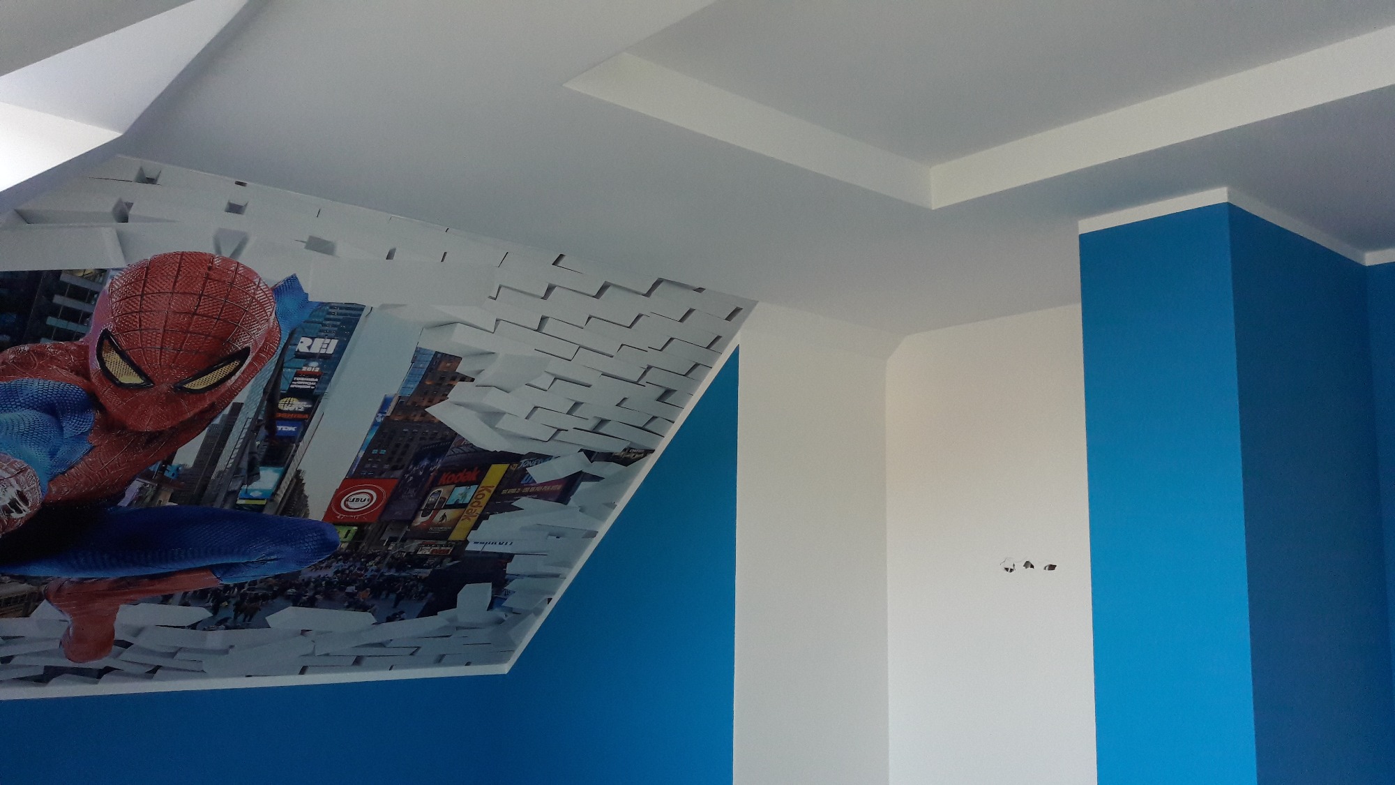 Pokój dziecięcy z fototapetą Spidermana na ścianie, niebieskie i białe ściany, biały sufit z dekoracyjną listwą.