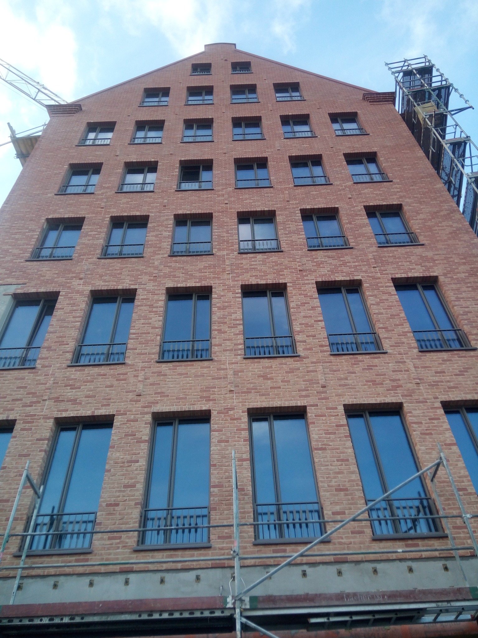 Wielopiętrowy budynek z cegły z licznymi oknami, widok z dołu, widoczne rusztowania.