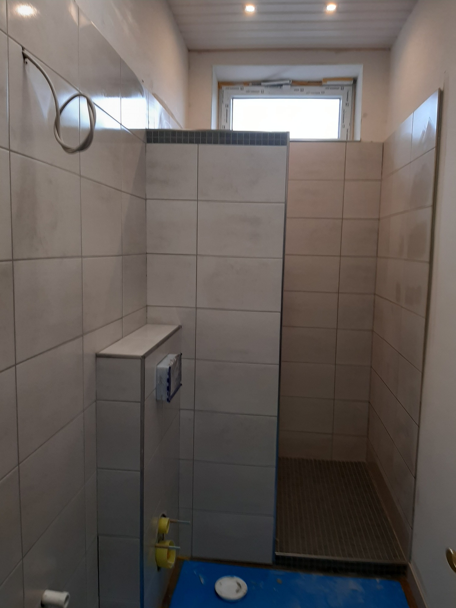 Wnętrze łazienki w trakcie remontu w Dąbrowie Górniczej, z widocznymi płytkami na ścianach, przygotowanym odpływem liniowym i instalacją podtynkową WC.