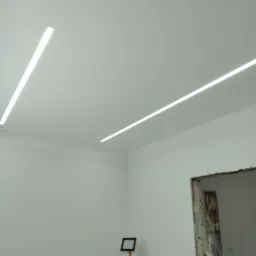 Nowoczesne oświetlenie liniowe LED na suficie w pomieszczeniu w trakcie remontu w Ozorkowie. Widoczne białe ściany i przygotowane do montażu ościeżnice.