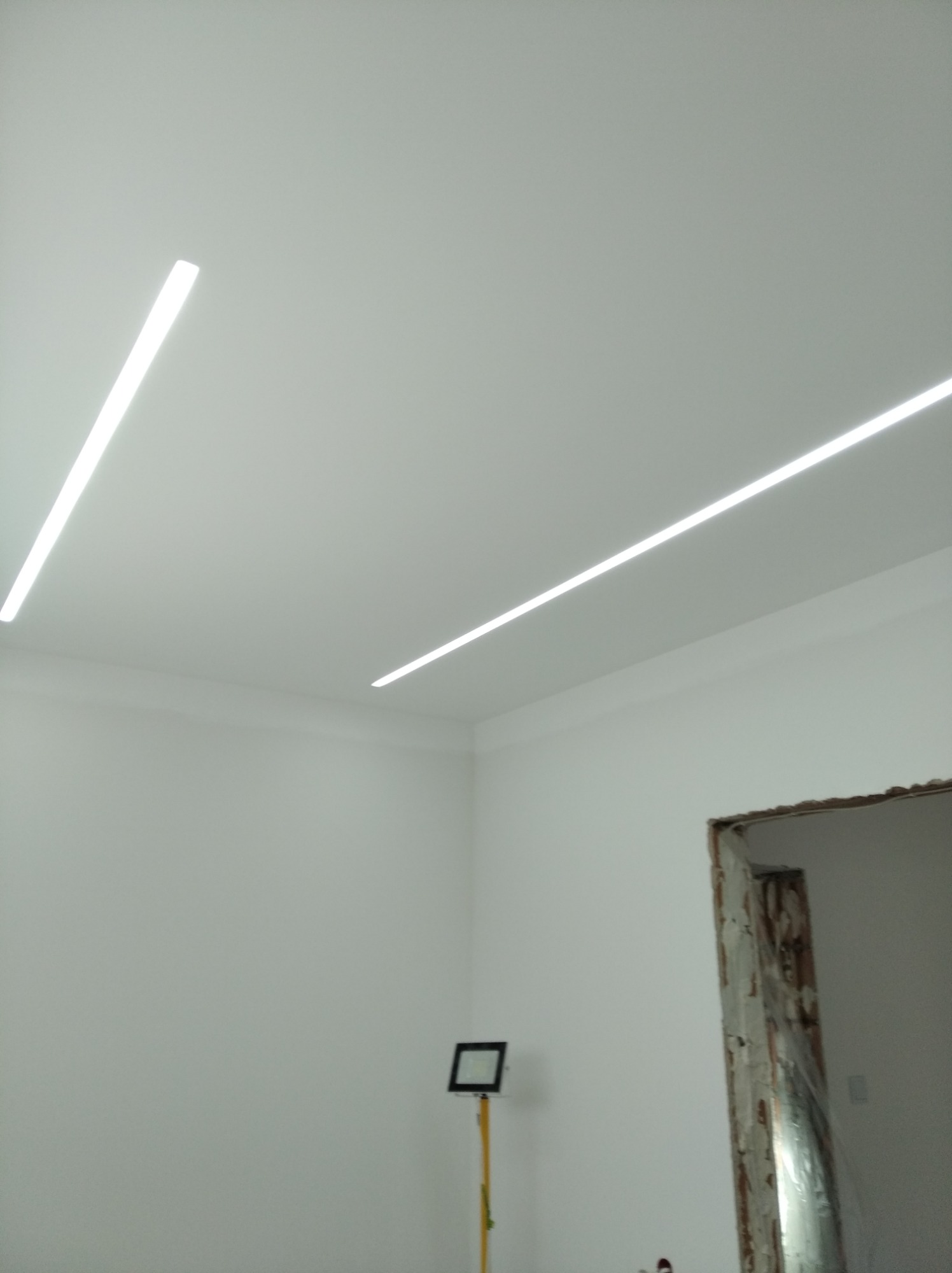 Nowoczesne oświetlenie liniowe LED na suficie w pomieszczeniu w trakcie remontu w Ozorkowie. Widoczne białe ściany i przygotowane do montażu ościeżnice.