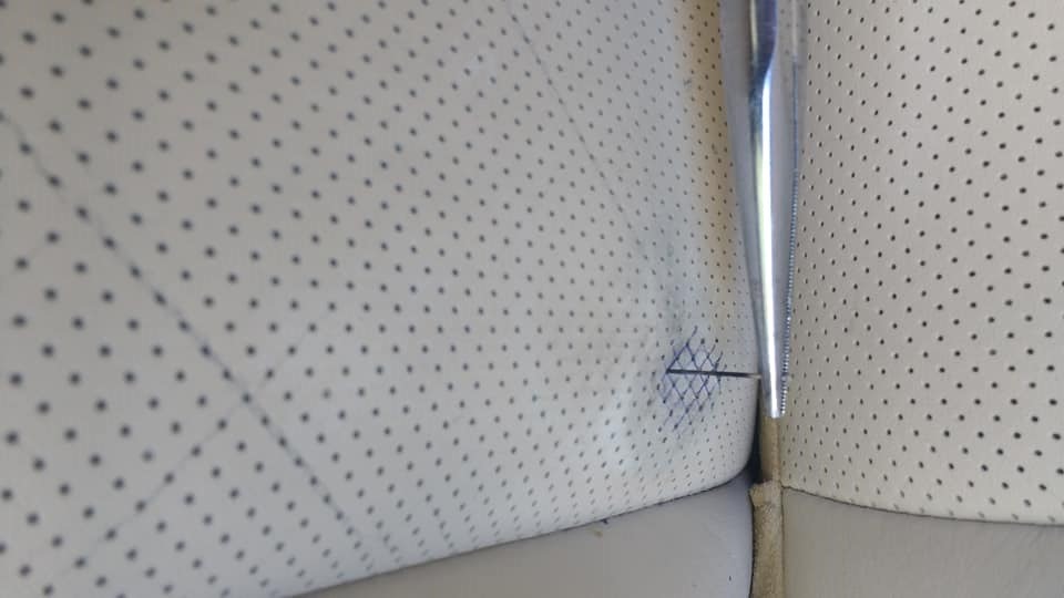 Igła i nitka naprawiająca rozdarcie w perforowanej, jasnej skórzanej tapicerce samochodowej, widoczne szwy.