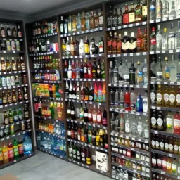 Półki wypełnione różnorodnymi butelkami alkoholi i napojów, od piw i wódek po likiery i soki, ułożone w uporządkowany sposób w przestronnym pomieszczeniu handlowym z szarymi ścianami.