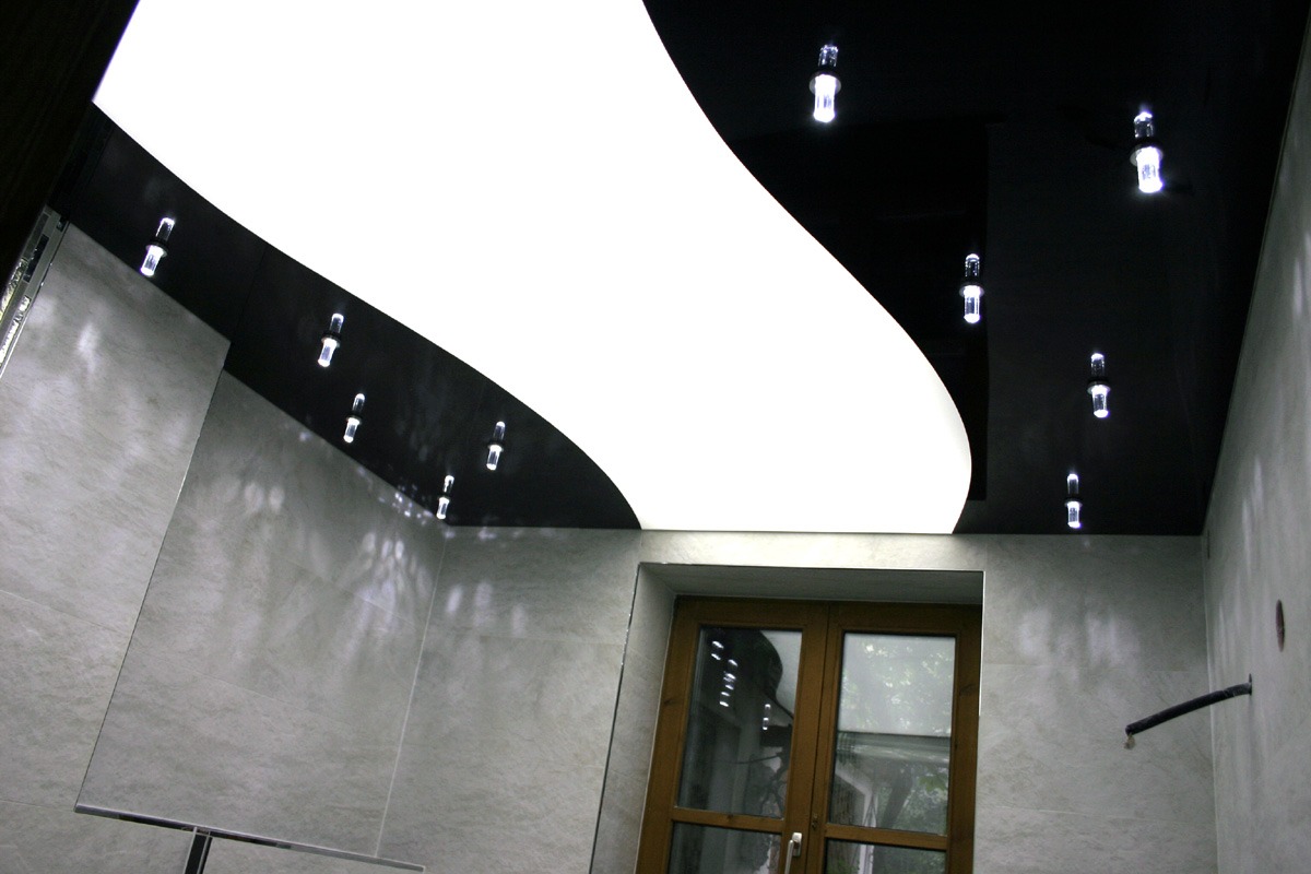 Nowoczesny sufit napinany z czarno-białym wzorem falistym i punktowym oświetleniem LED w łazience z szarymi płytkami.