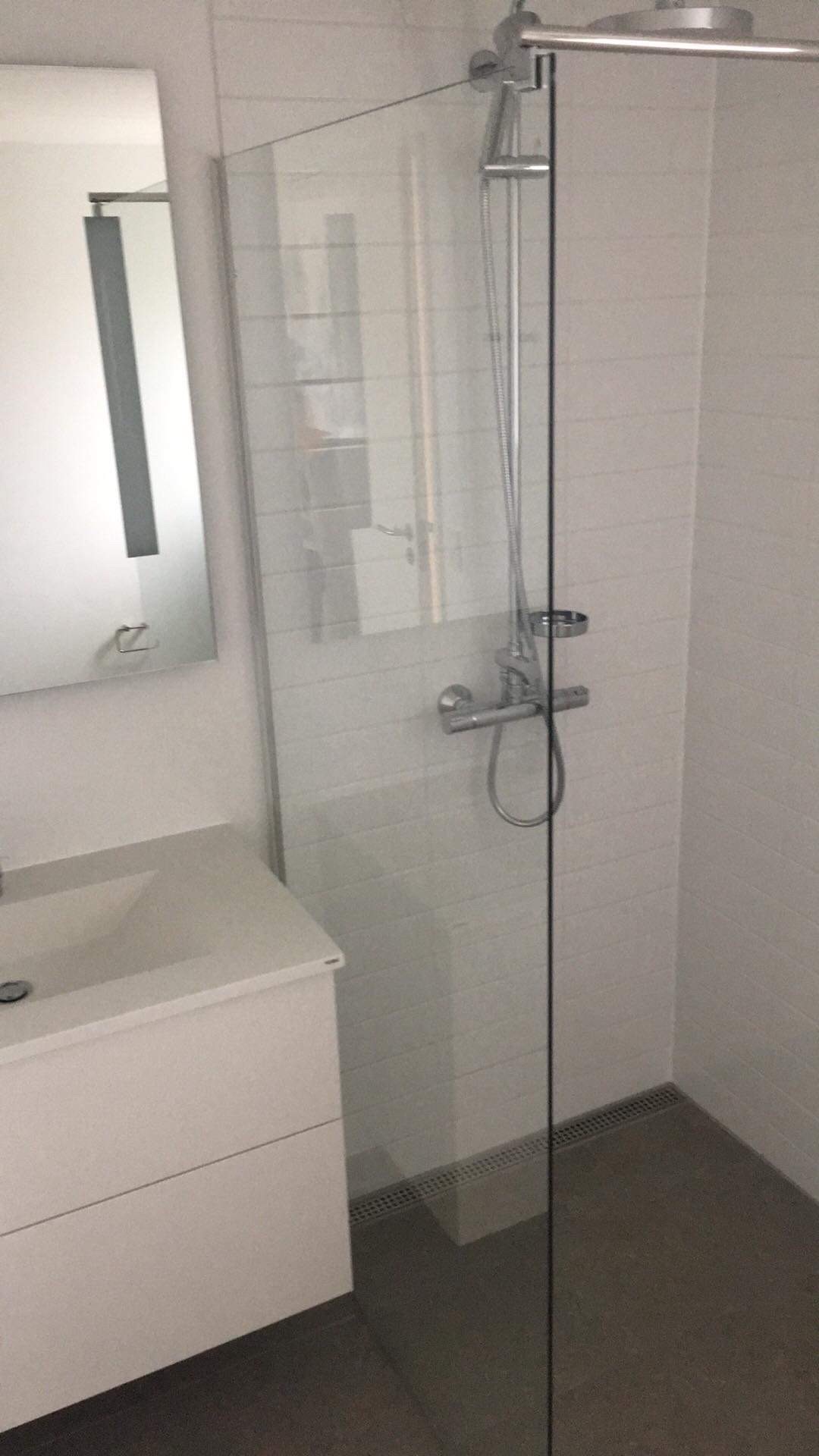 Nowoczesna kabina prysznicowa ze szklaną ścianką i odpływem liniowym w wykończonej łazience w Warszawie, widoczna umywalka z szafką i lustro.