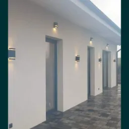 Elewacja budynku z zamontowanymi, nowoczesnymi lampami zewnętrznymi o prostokątnym kształcie, oświetlającymi wejścia.