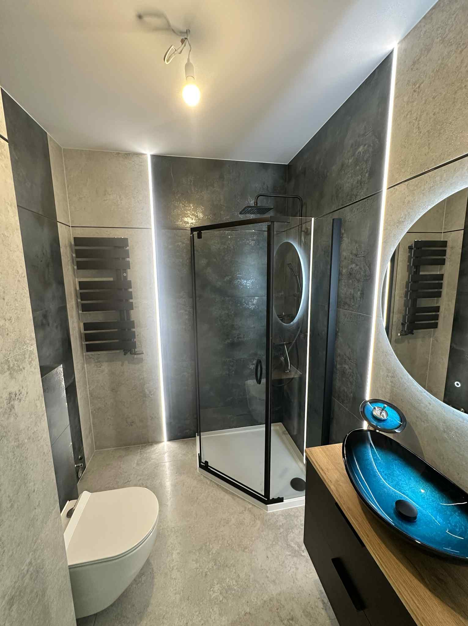 Nowoczesna łazienka w szarościach z akcentem turkusowej umywalki, kabiną prysznicową typu walk-in i podświetlanym lustrem. Minimalistyczny design, grzejnik drabinkowy.