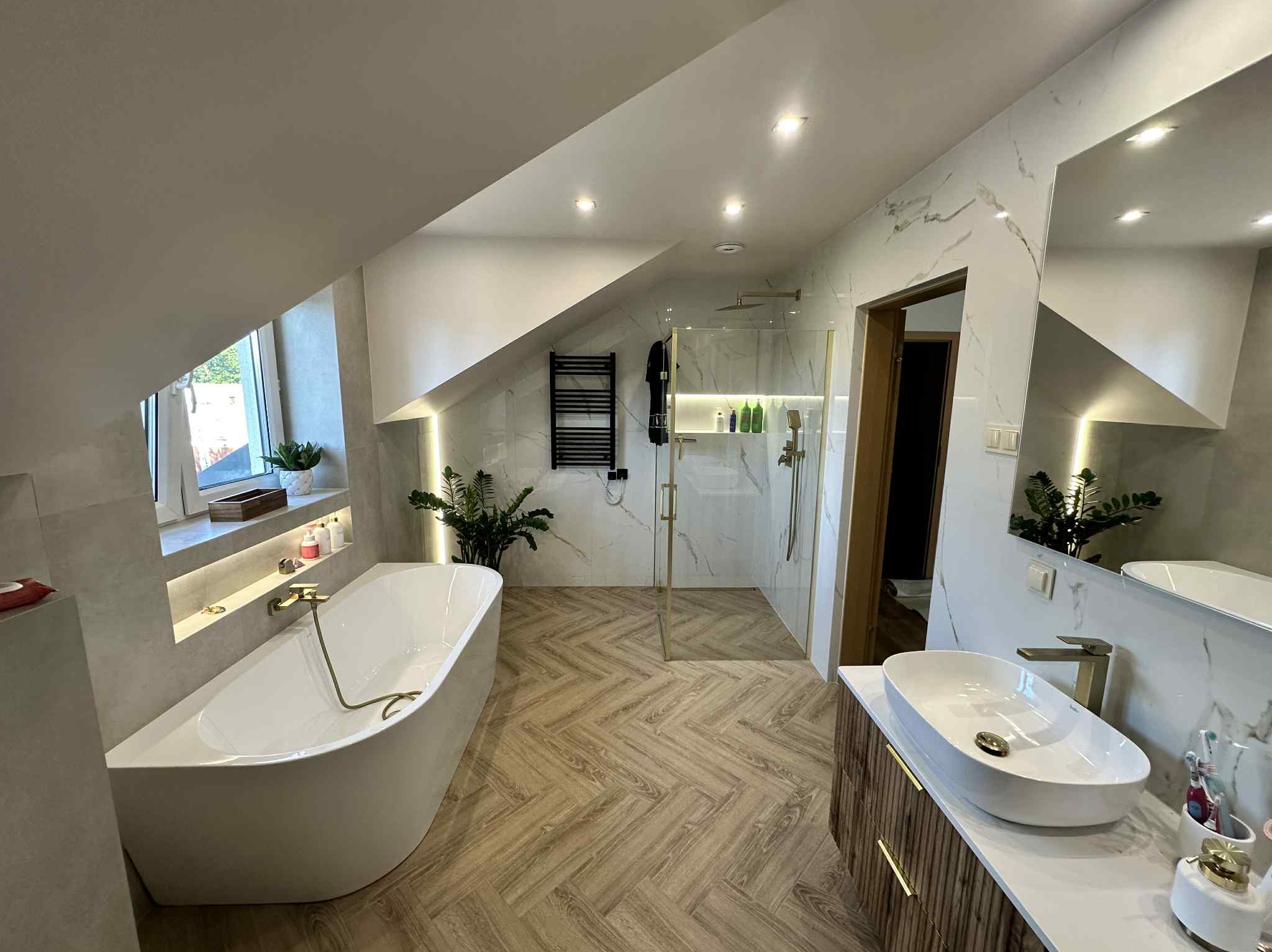 Elegancka łazienka na poddaszu z wanną wolnostojącą, kabiną prysznicową typu walk-in, umywalką nablatową i drewnopodobną podłogą ułożoną w jodełkę.
