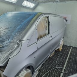 2KB AUTO DETAILING - Pół-matowy, srebrny van w kabinie lakierniczej, częściowo zakryty folią ochronną przed lakierowaniem.