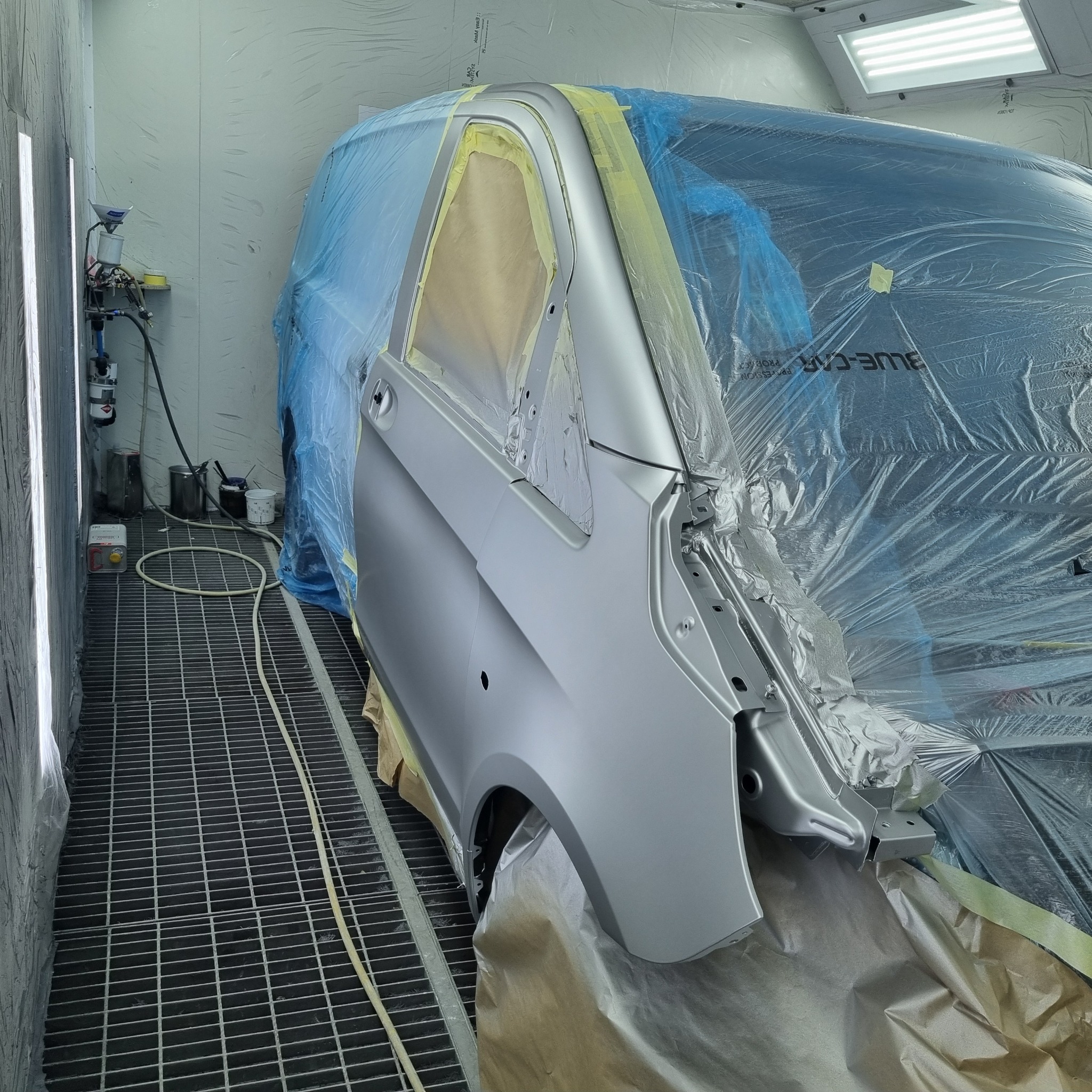 Element karoserii samochodu (drzwi) po lakierowaniu w kabinie lakierniczej, zabezpieczony folią i taśmą maskującą.