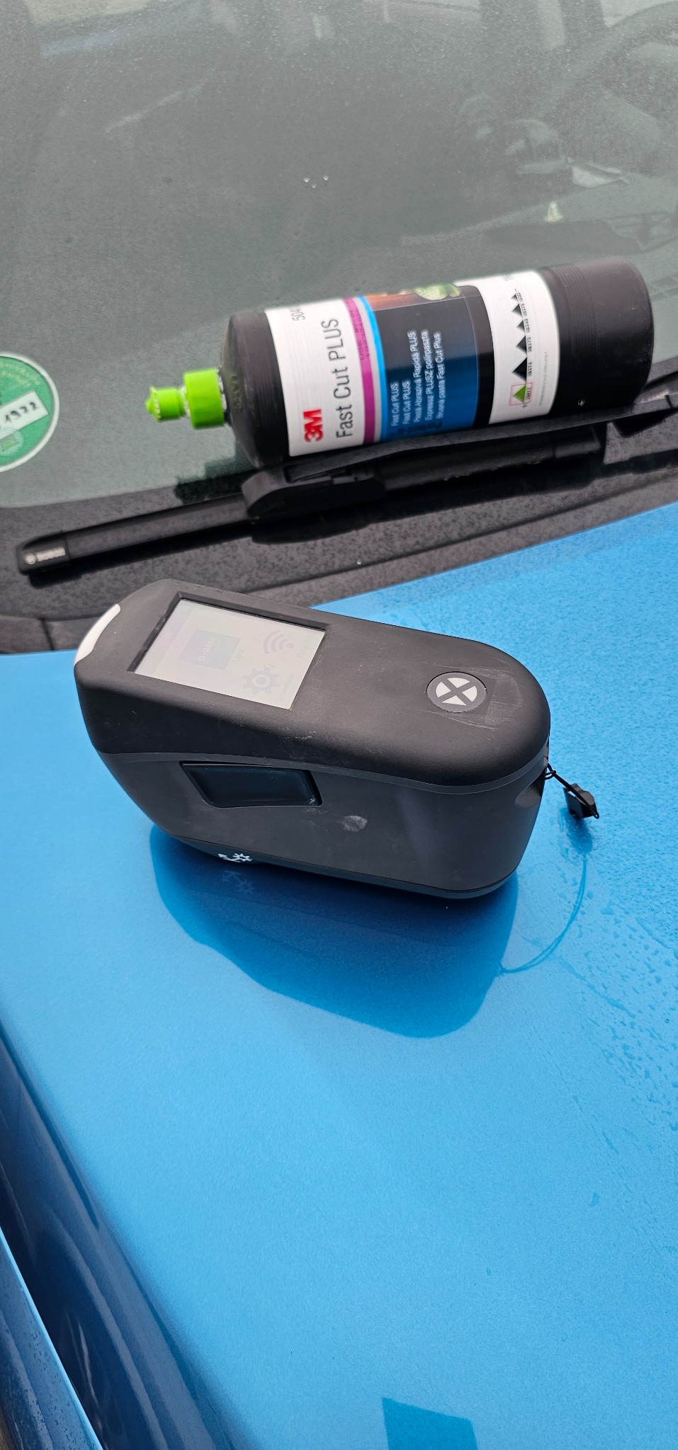 Miernik koloru lakieru samochodowego i butelka pasty polerskiej 3M Fast Cut Plus na niebieskiej karoserii auta.