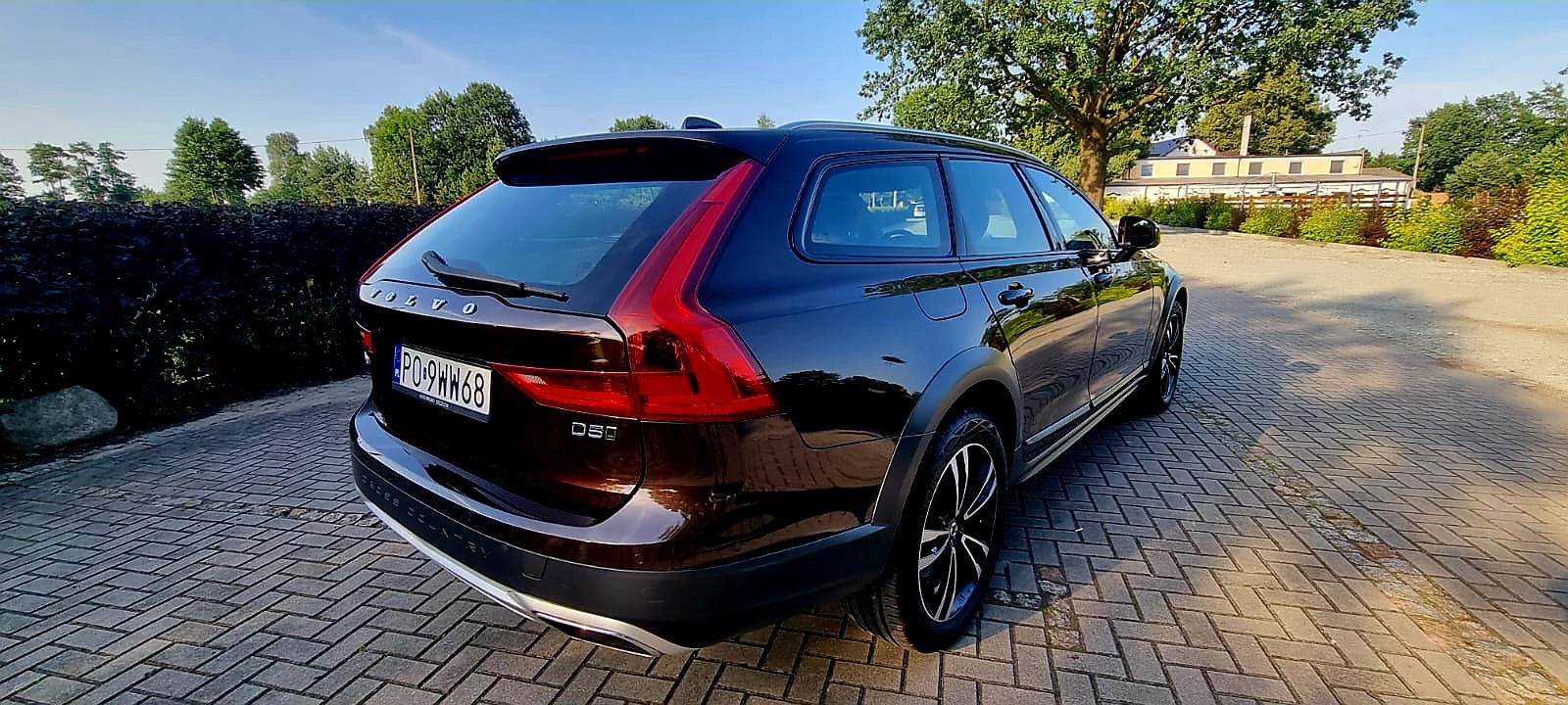 Ciemnobrązowe Volvo V60 Cross Country zaparkowane na brukowanej nawierzchni, widok z tyłu, z widocznymi elementami karoserii i oponami terenowymi.