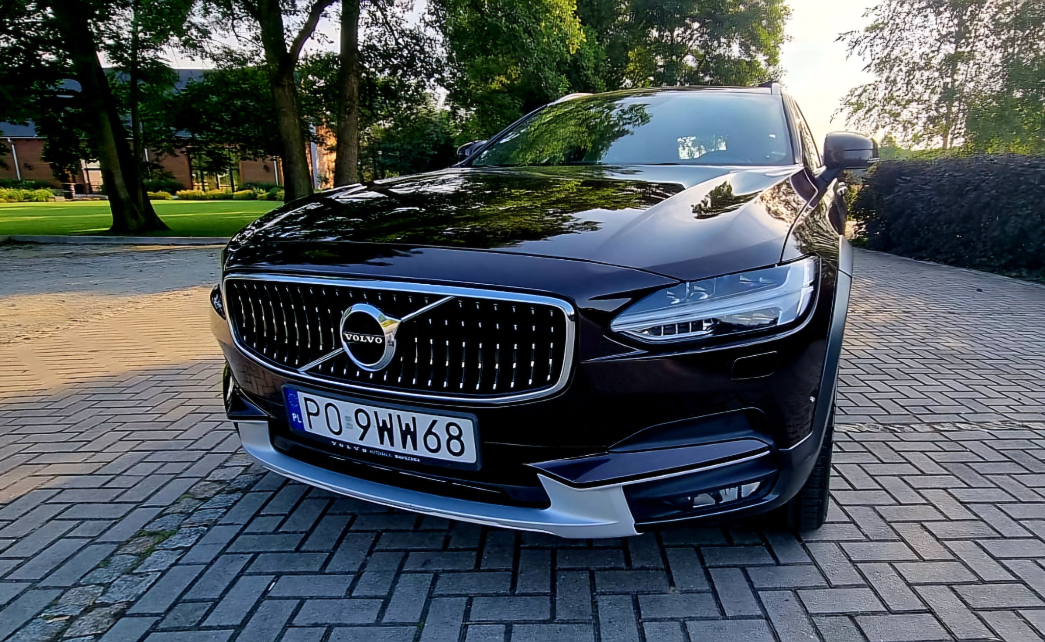 Czarny samochód marki Volvo, widok z przodu na tle brukowanej drogi i zieleni.