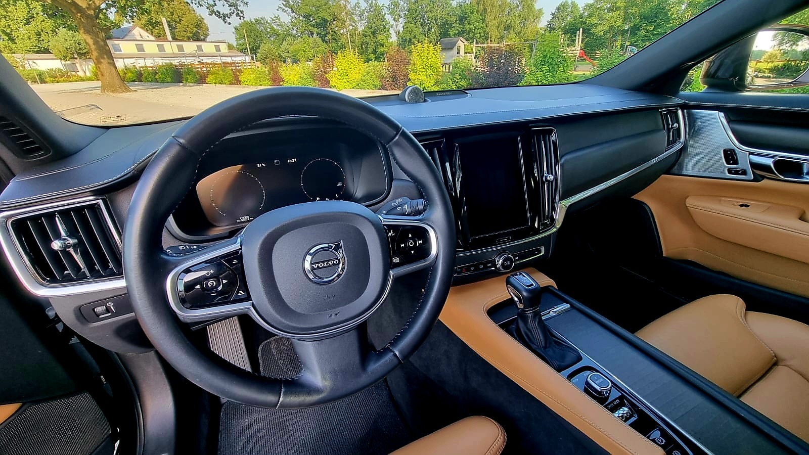 Wnętrze luksusowego samochodu Volvo z beżową skórzaną tapicerką, widok na deskę rozdzielczą, kierownicę z logo Volvo i cyfrowy wyświetlacz.