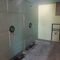 Instal-Tech Arkadiusz Miś - Wnętrze łazienki w trakcie montażu instalacji ogrzewania podłogowego; widoczne rury grzewcze rozłożone na folii izolacyjnej, ściany wyłożone płytami gipsowo-kartonowymi z przygotowanymi otworami...