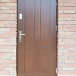 Brązowe drzwi wejściowe z czterema panelami w ceglanej ścianie, z widoczną klamką i zamkiem.