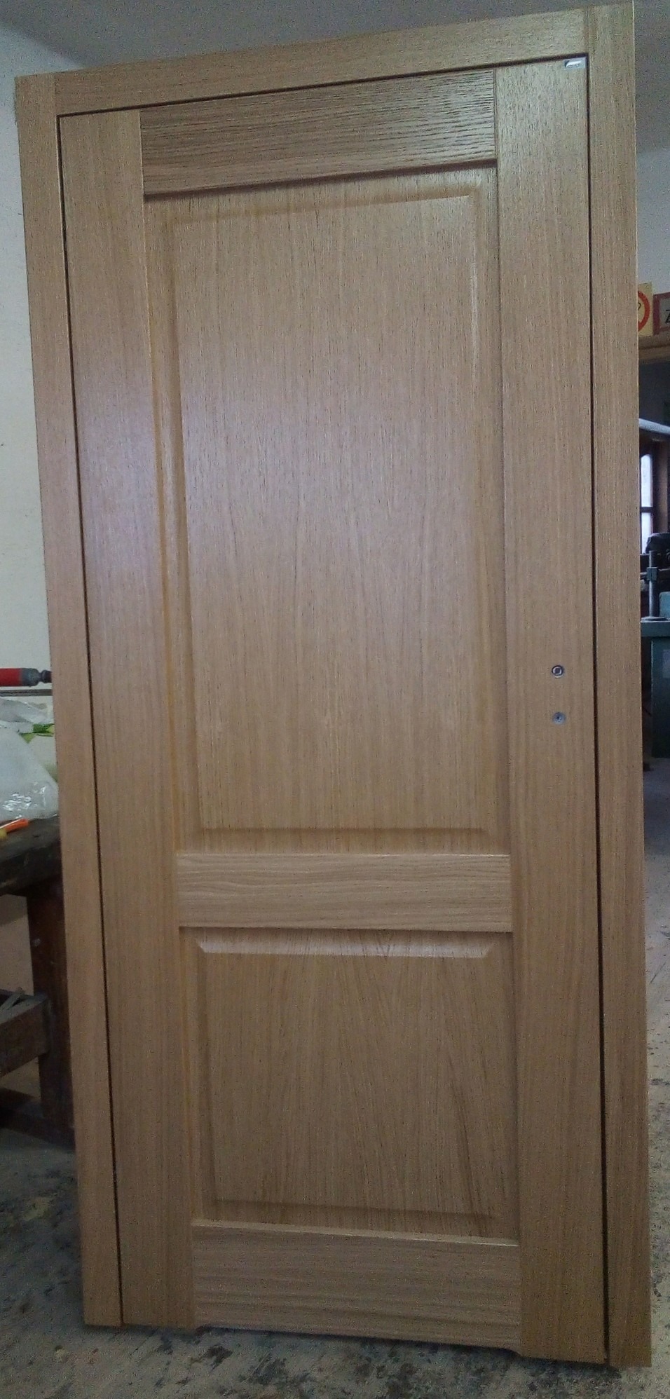 Klasyczna, dębowa konstrukcja drzwiowa z dwoma panelami, widoczne delikatne usłojenie drewna i dwa otwory na klamkę, w tle warsztat stolarski.