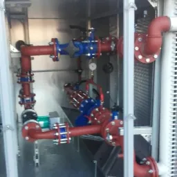 Złożona instalacja rur z zaworami i manometrem wewnątrz metalowej obudowy, widoczne elementy systemu chłodzenia