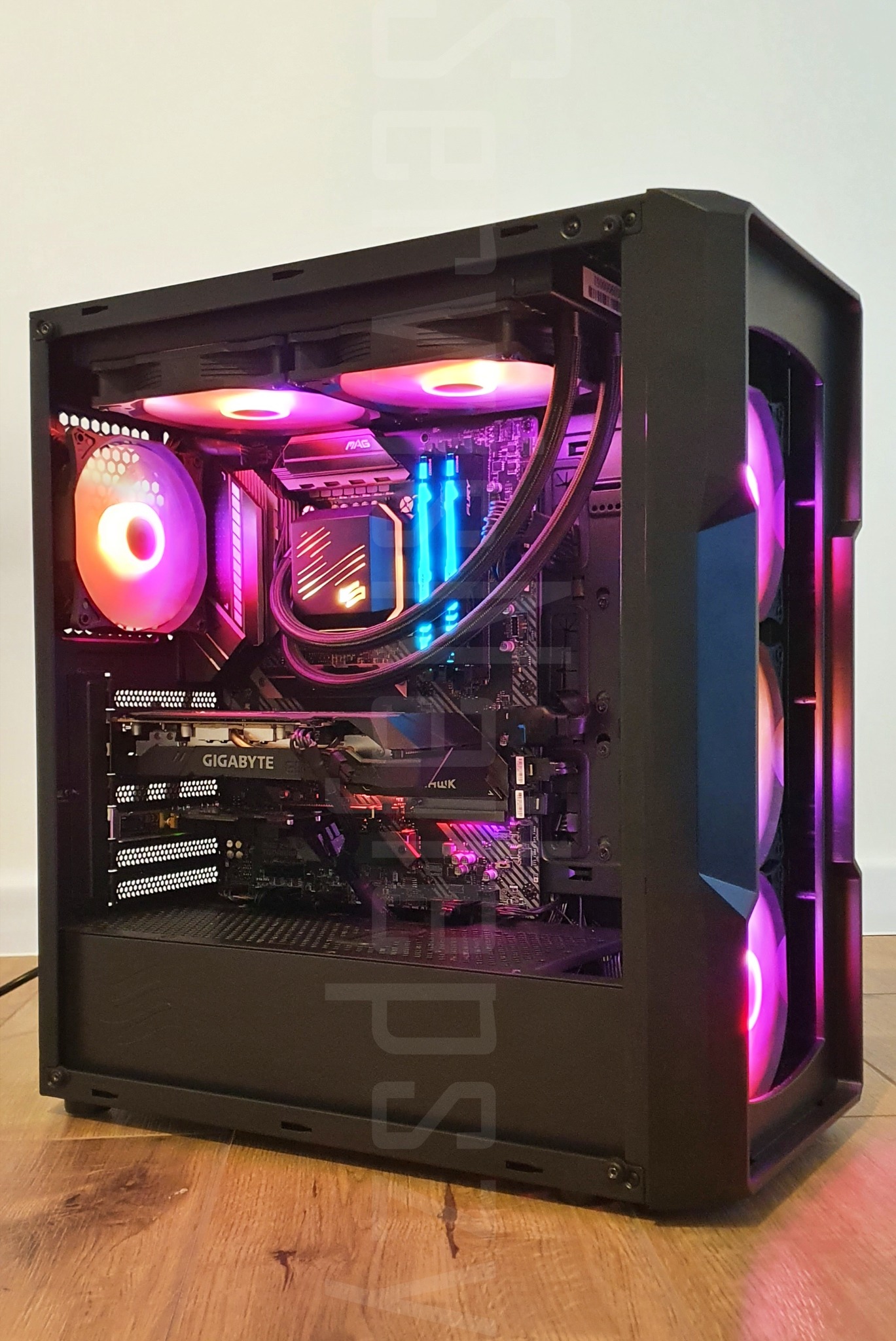 Otwarta obudowa komputera stacjonarnego z widocznymi podzespołami oświetlonymi diodami RGB, w tym karta graficzna Gigabyte, chłodzenie wodne procesora i wentylatory z tęczowym podświetleniem...