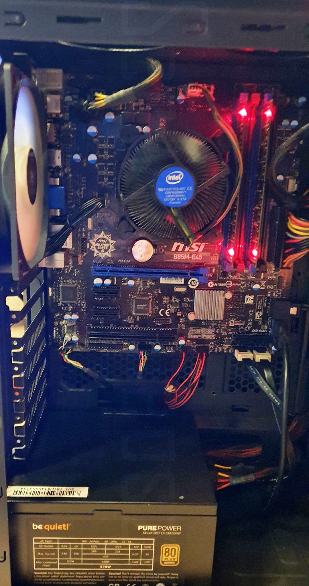 Wnętrze obudowy komputera stacjonarnego z widoczną płytą główną MSI B85M-E45, chłodzeniem procesora Intel, pamięcią RAM z czerwonym podświetleniem i zasilaczem be quiet! Pure Power 530W.