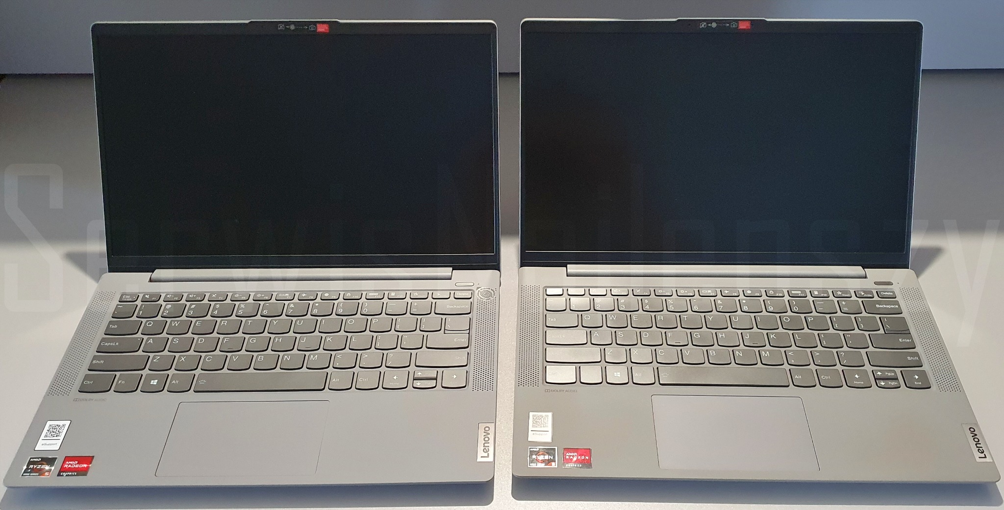 Dwa identyczne, szare laptopy Lenovo z zamkniętymi ekranami, ustawione obok siebie na jasnym tle, z widocznymi naklejkami AMD Ryzen i Radeon Graphics.