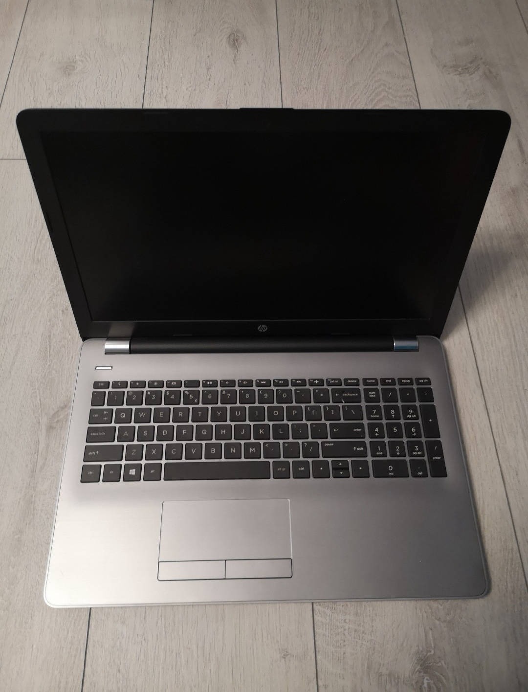 Otwarty srebrny laptop HP z czarnym ekranem i klawiaturą na jasnym drewnianym tle.