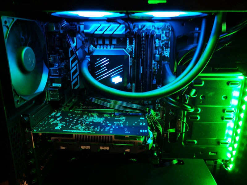 Wnętrze komputera stacjonarnego z chłodzeniem wodnym, podświetlone na niebiesko i zielono, widoczna karta graficzna i płyta główna.