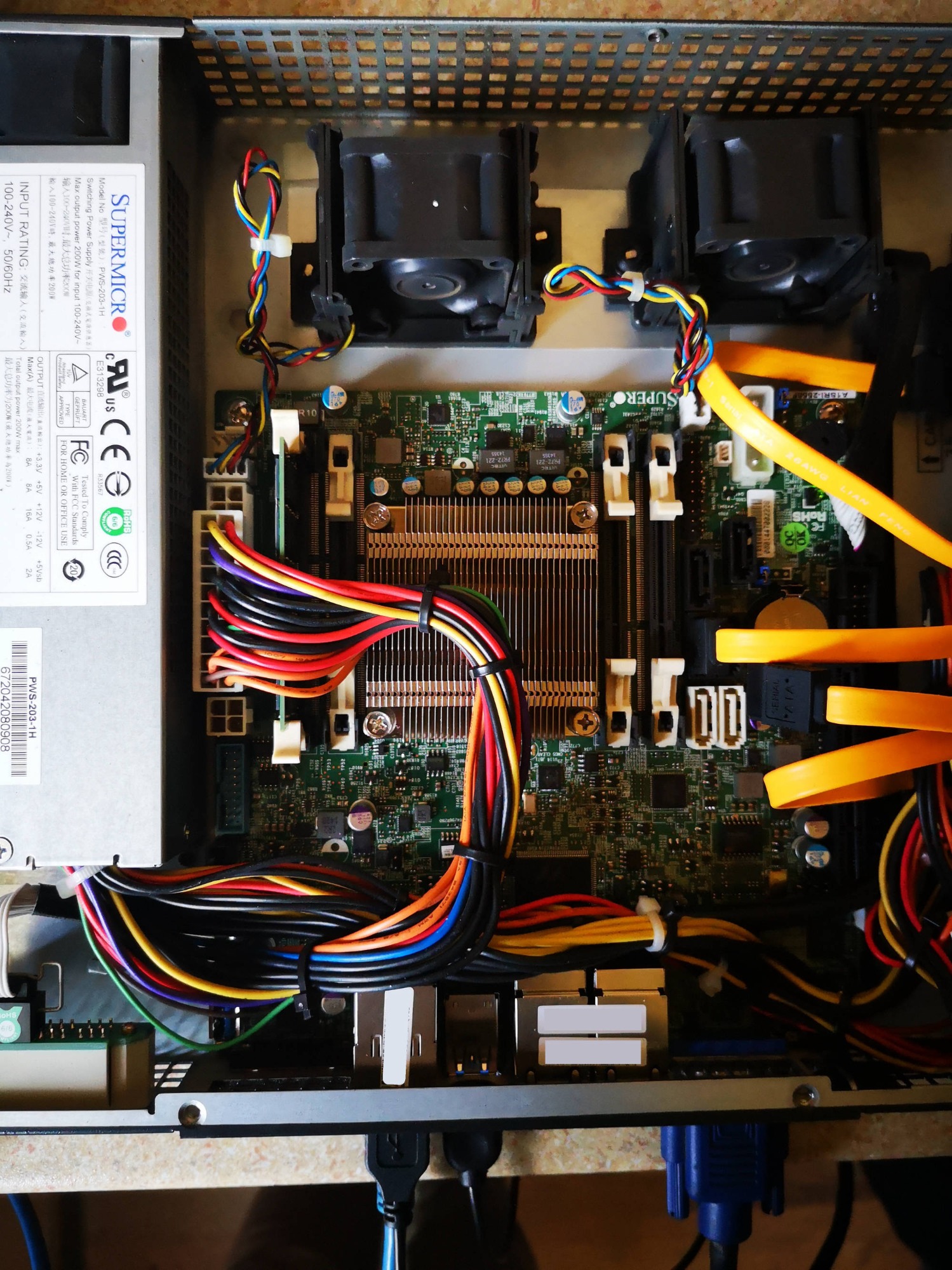 Otwarta obudowa serwera z widoczną płytą główną, procesorem z radiatorem, wentylatorami, zasilaczem Supermicro i wiązkami kolorowych kabli w Czechowicach-Dziedzicach. Żółte kable SATA prowadzą...