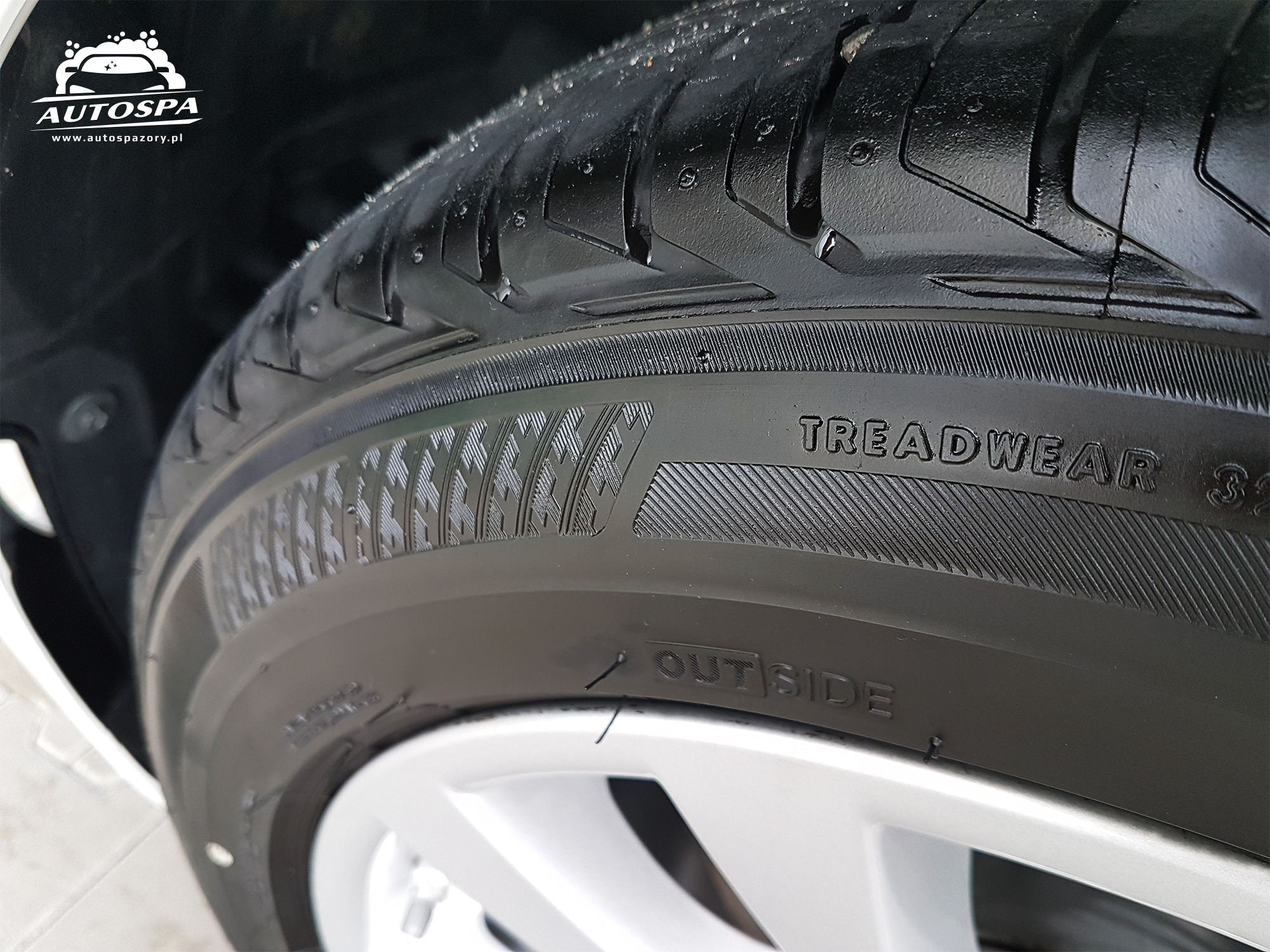 Błyszcząca, czysta opona samochodowa z widocznym bieżnikiem i napisem TREADWEAR, po umyciu w myjni, z bliska.