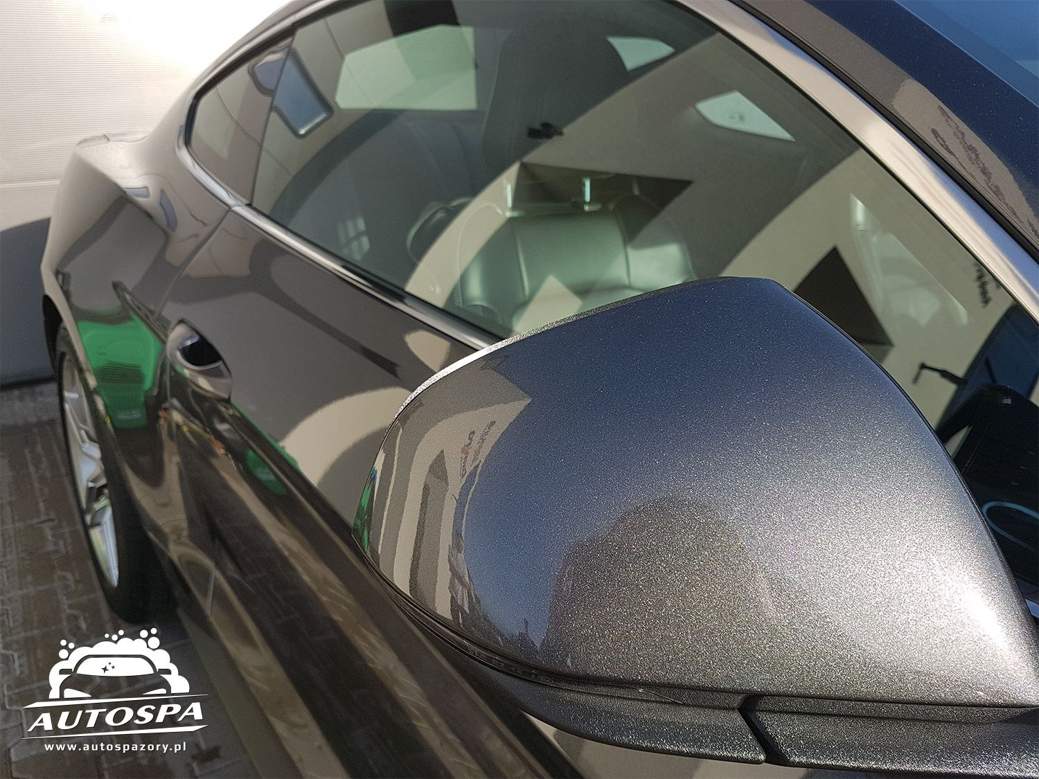 Błyszczący, szary samochód po umyciu, widoczne odbicia w lakierze, z logo firmy Autospa w lewym dolnym rogu.
